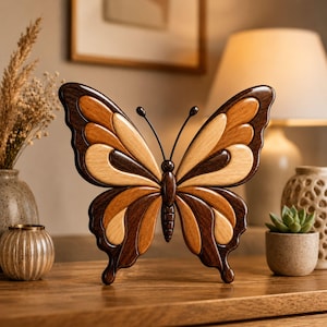 Peut inclure: Sculpture en bois en forme de papillon, avec un design en couches dans des tons bruns et beiges. Le papillon présente des bords brun foncé et des sections en bois plus claires. Il est posé sur une surface en bois.