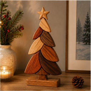 May include: A decorative wooden Christmas tree sculpture composed of stacked, leaf-shaped segments in varying shades of brown, ranging from light tan to dark walnut. The tree is topped with a five-pointed star and stands on a rectangular base.
