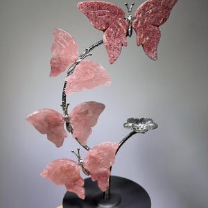 A hand is holding a decorative piece featuring a butterfly and a flower, with the butterfly being the main focus.
