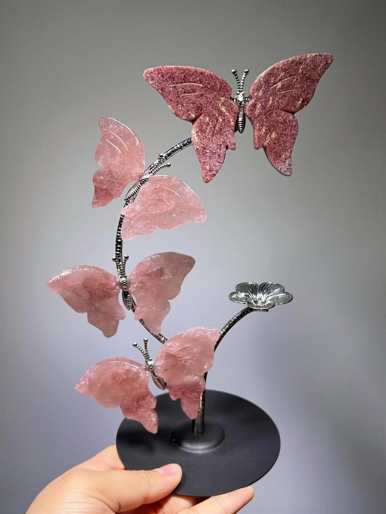 A hand is holding a decorative piece featuring a butterfly and a flower, with the butterfly being the main focus.