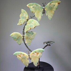 A hand is holding a decorative sculpture of green and yellow butterfly-shaped objects, which appear to be made of a material that resembles stone or glass.