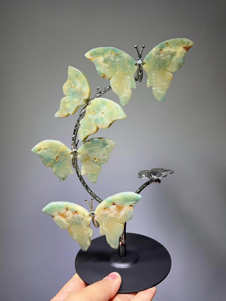 A hand is holding a decorative sculpture of green and yellow butterfly-shaped objects, which appear to be made of a material that resembles stone or glass.