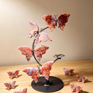 a decorative sculpture of butterflies, with a total of 14 butterflies displayed on a wooden surface. The butterflies are painted in shades of red and orange and are arranged in a circular pattern around a black base.
