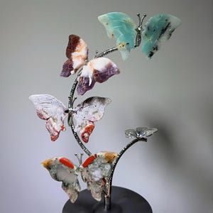 A hand is holding a decorative sculpture of colorful butterflies on a black base.