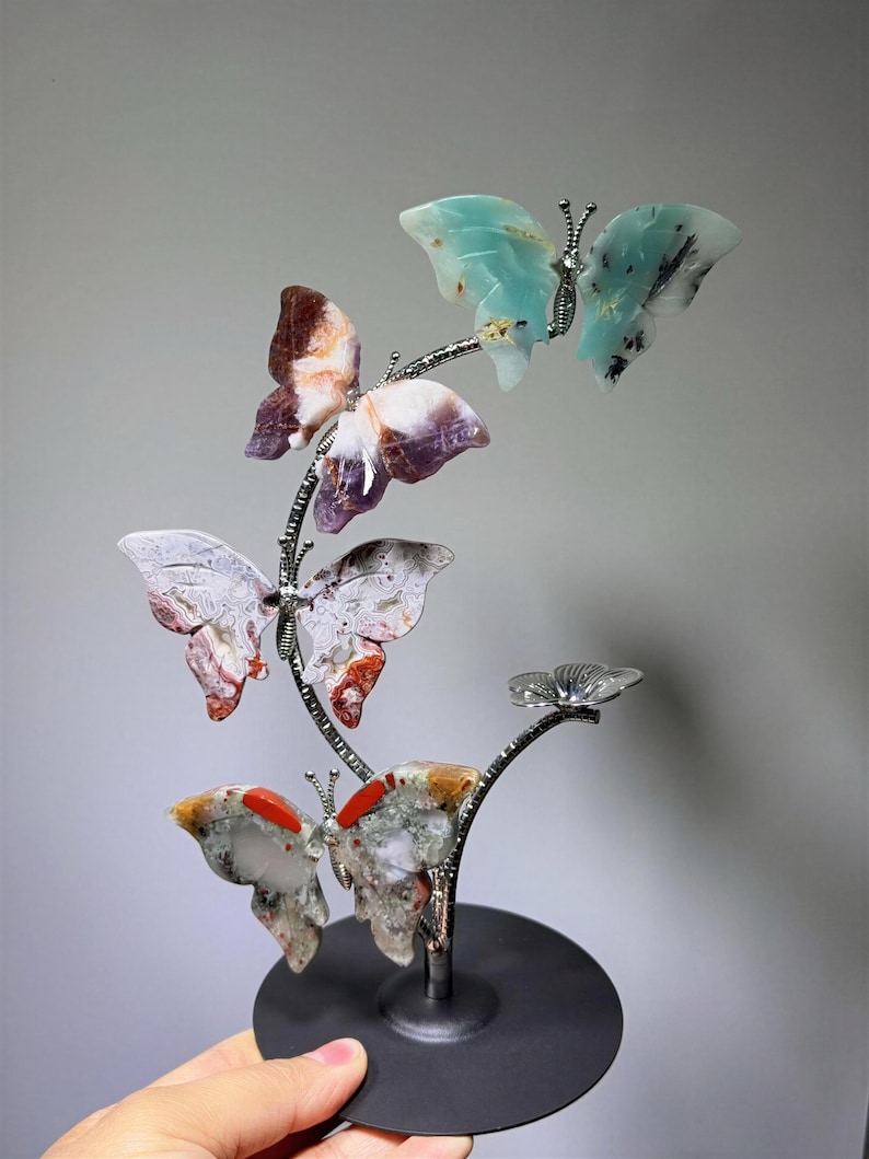 A hand is holding a decorative sculpture of colorful butterflies on a black base.