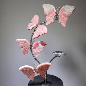 A hand is holding a decorative sculpture of pink and white butterflies on a black base.