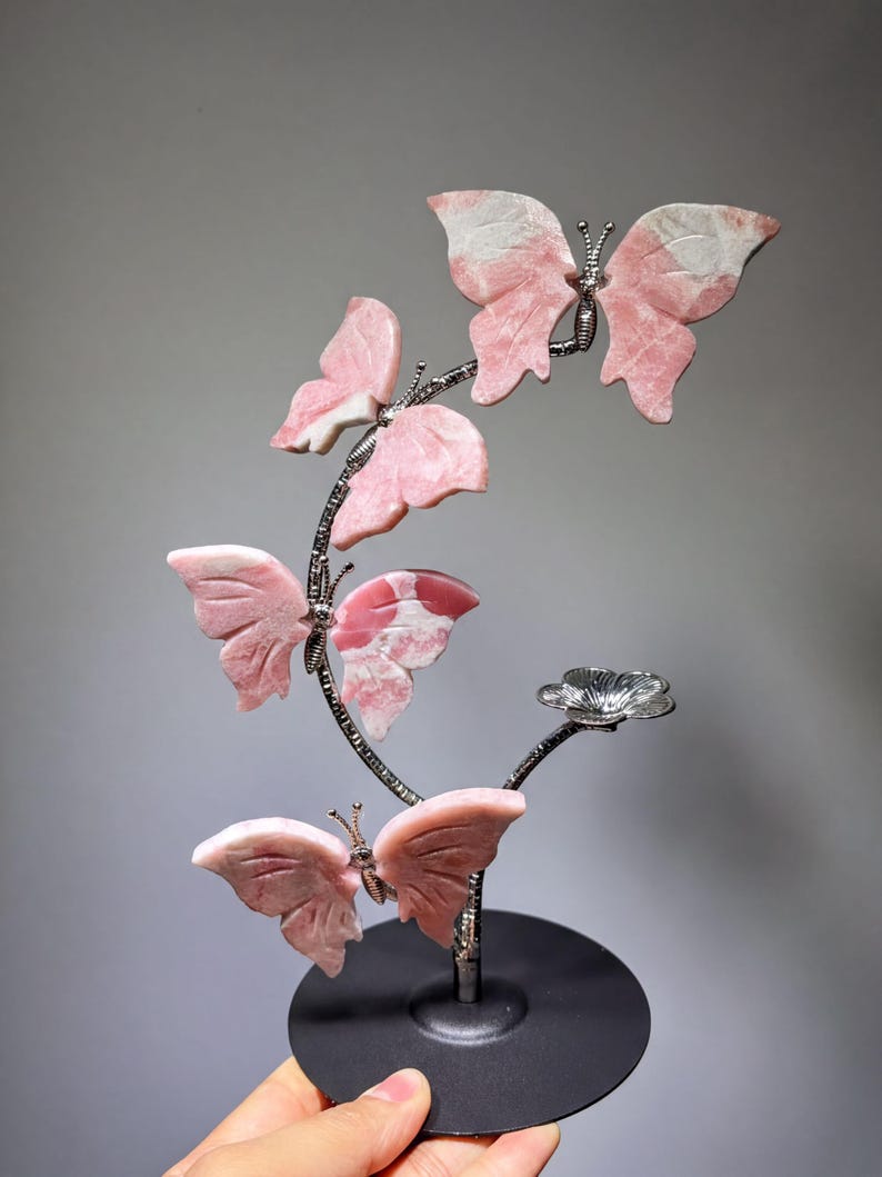 A hand is holding a decorative sculpture of pink and white butterflies on a black base.