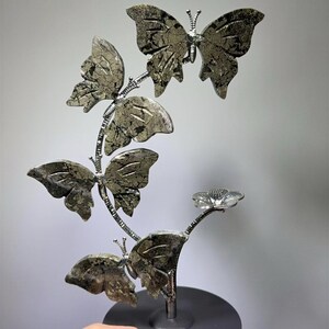 A hand is holding a decorative sculpture of a butterfly, which is made of a shiny material and has a floral design.