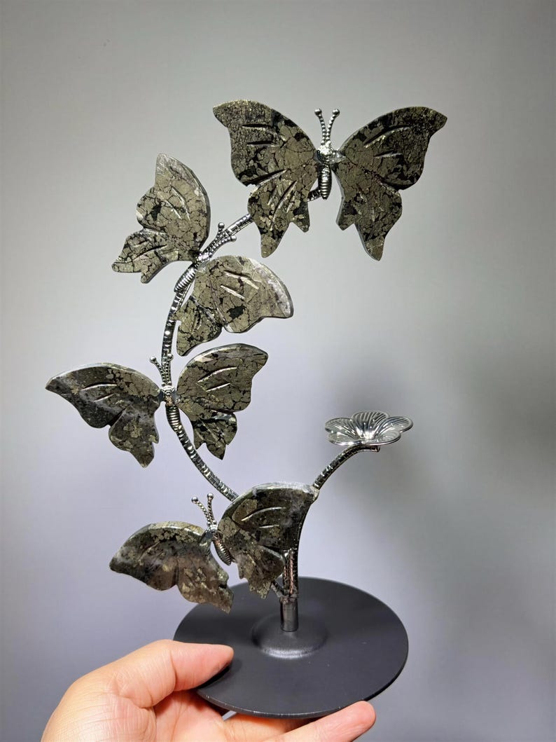 A hand is holding a decorative sculpture of a butterfly, which is made of a shiny material and has a floral design.