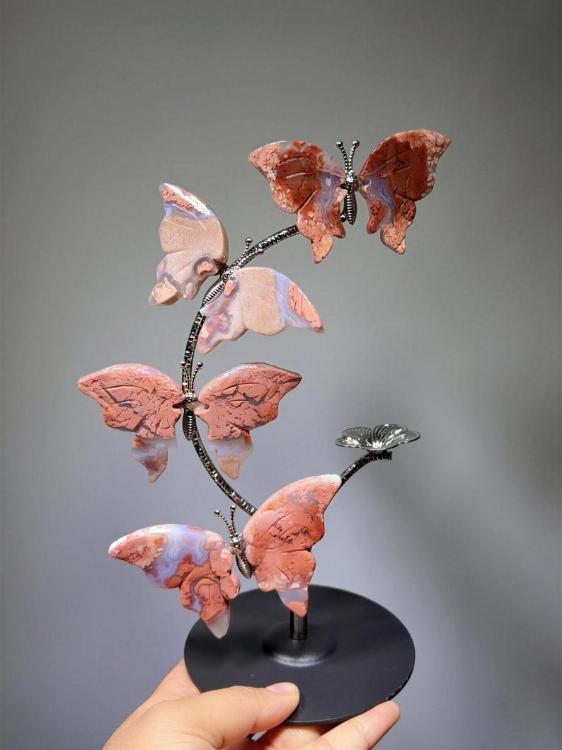A hand is holding a decorative sculpture of butterflies on a black base.