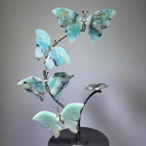 A hand is holding a decorative sculpture of blue and green butterflies on a black base.