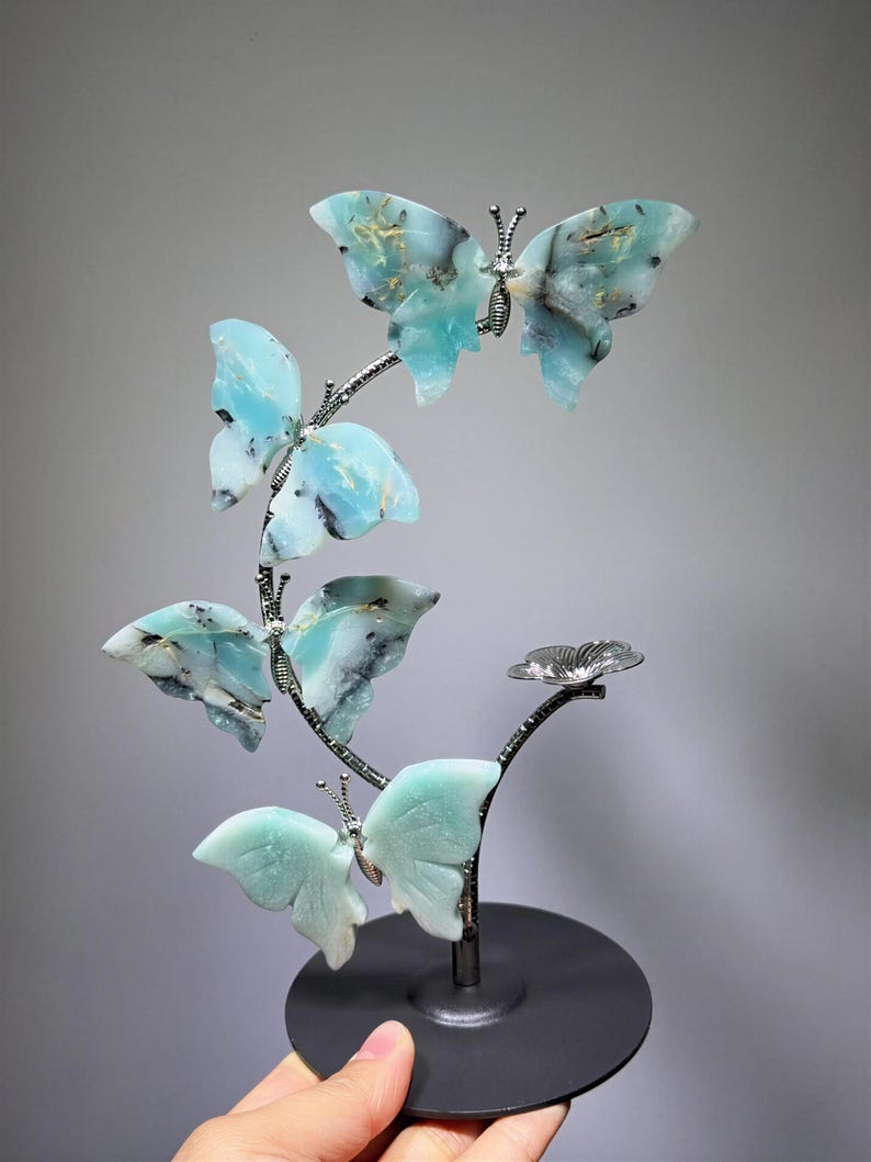 A hand is holding a decorative sculpture of blue and green butterflies on a black base.