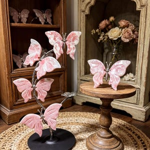 a decorative arrangement of pink butterfly figurines on a wooden stand, with a vase of flowers in the background.