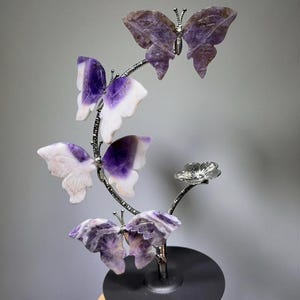 A hand is holding a decorative piece featuring a branch with purple and white butterfly-shaped ornaments.