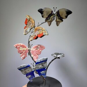 A hand is holding a decorative sculpture of colorful butterflies on a black base.