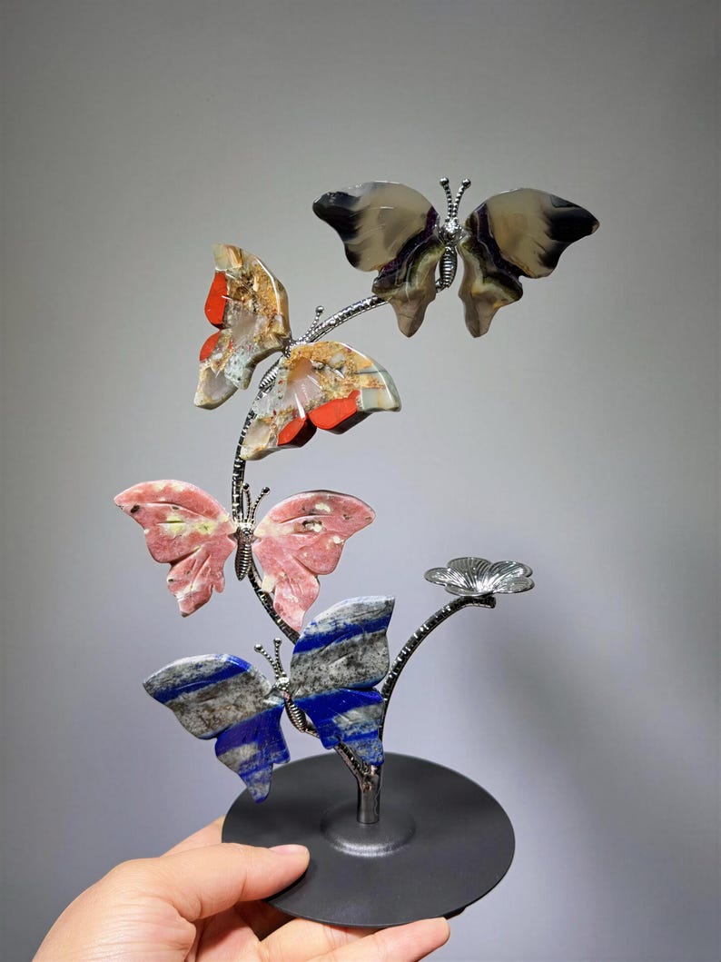 A hand is holding a decorative sculpture of colorful butterflies on a black base.