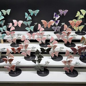 a display of various colorful butterfly figurines arranged on a white shelf against a black background.