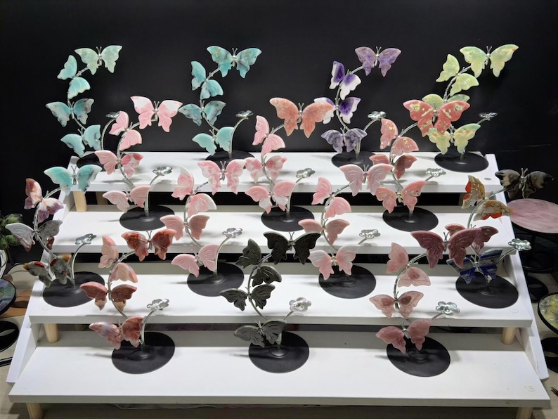 a display of various colorful butterfly figurines arranged on a white shelf against a black background.