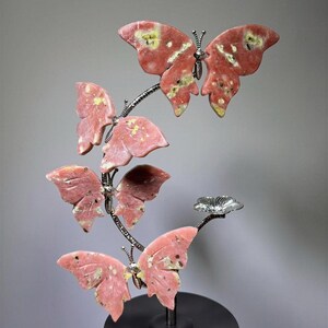 A hand is holding a decorative sculpture of pink butterflies on a black base.