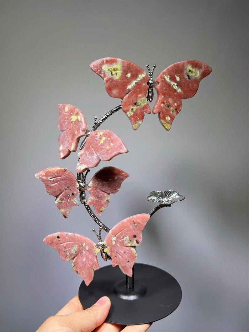 A hand is holding a decorative sculpture of pink butterflies on a black base.