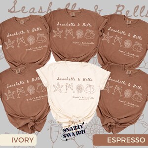 Peut inclure: Plusieurs t-shirts de couleur ivoire et expresso. Chaque t-shirt porte l'inscription "Seashells & Bells" avec des graphiques d'étoiles de mer, de flûtes à champagne, d'un coquillage et d'une cloche. Le texte "Taylor's Bachelorette Miami Beach, FL" est également imprimé.