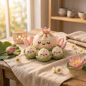 May include: A set of crocheted plush toys featuring one large cream-colored bun with a pink lotus flower on top and three smaller matching buns, each nestled in a green crocheted base. The buns have embroidered closed eyes and smiling mouths.