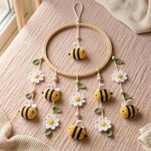 May include: A handcrafted baby mobile with a wooden ring, crocheted bees and daisies. The bees are yellow and black, and the daisies are white with yellow centres. The mobile is suspended from a loop and adorned with wooden beads and green leaves.