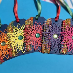 May include: Five rectangular navy blue cardstock tags, each featuring a die-cut flower in orange, yellow, red, purple, or pink. Each flower has a central gemstone and is accented with a vertical strip of metallic gold, blue, and red trim.
