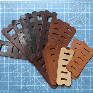 Puede incluir: Una colección de correas de cuero en varios tonos de marrón, dispuestas en forma de abanico. Las correas tienen recortes rectangulares y probablemente son para proyectos de artesanía o marroquinería. Los colores varían de marrón claro a marrón oscuro.