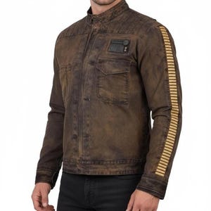 May include: Brown jacket with a stand-up collar, two chest pockets, and a small patch on the upper left chest. The sleeves have a series of vertical gold stripes. The jacket has a distressed, vintage look.