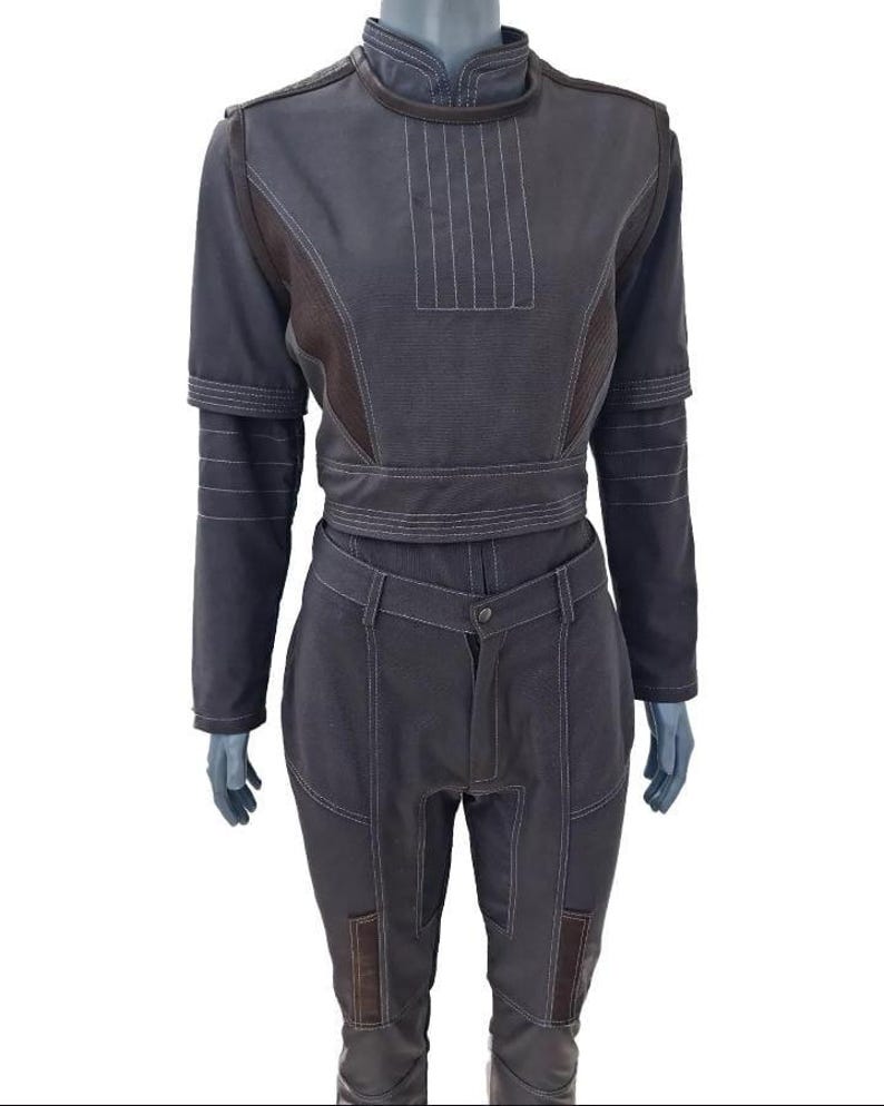 Puede incluir: Un conjunto de dos piezas en gris carb&oacute;n oscuro que consta de una parte superior de manga larga con cuello alto y pantalones a juego. La parte superior presenta detalles de costuras verticales en el pecho y los hombros. Los pantalones tienen cierre de bot&oacute;n y paneles reforzados en las piernas con costuras visibles de color claro en toda la prenda.