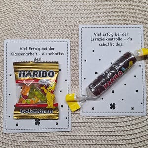 May include: Two cards with the text "Viel Erfolg bei der Klassenarbeit - du schaffst das!" and "Viel Erfolg bei der Lernzielkontrolle - du schaffst das!". One card has a bag of Haribo gummy bears, the other has a Haribo candy roll.