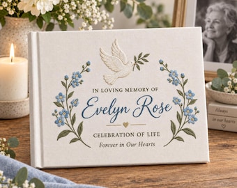 Könnte beinhalten: Ein weißes Gedenkbuch mit einer gestickten Taube und blauen Blumen. Der Text lautet: IN LOVING MEMORY OF Evelyn Rose CELEBRATION OF LIFE Forever in Our Hearts. Ein kleines goldenes Herz befindet sich unter dem Namen auf dem Stoffeinband.
