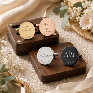 May include: Four circular cufflinks in gold, rose gold, silver, and black metal finishes. The gold cufflink reads A and J 12.09.23, the rose gold reads My heart is yours forever, the silver reads a r AUGUST 31, 2021, and the black reads A M MAY 05TH, 2023.