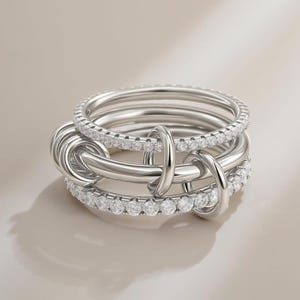 May include: A silver ring set with multiple interlocking bands. One band is adorned with small, clear gemstones. The design is contemporary and stylish, suitable for everyday wear or special events.