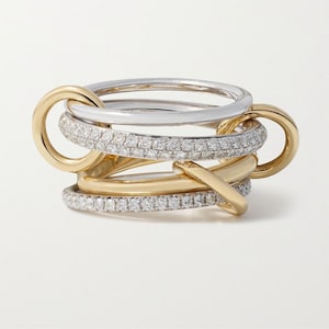 May include: An intricate ring featuring a multi-band design. The ring combines gold and silver bands, with one band encrusted with small, sparkling stones. The bands are interlocked, creating a unique and elegant look.