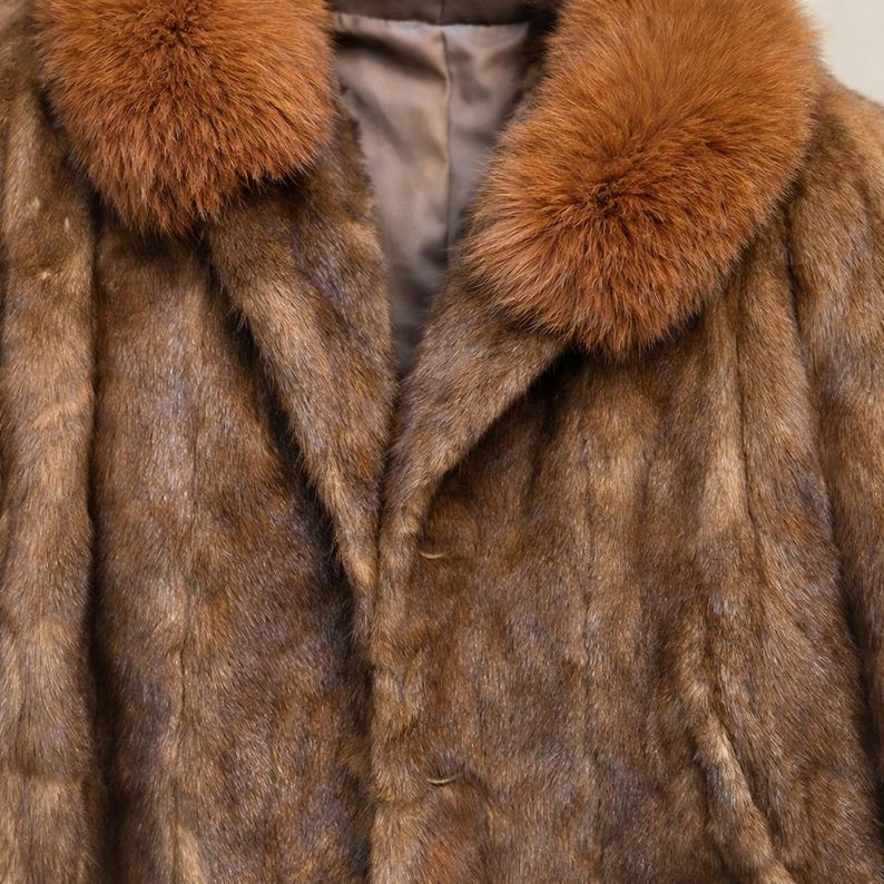 May include: A brown fur coat with a reddish-brown fur collar. The coat has a button closure and a silky lining. The fur appears soft and luxurious, with a natural sheen. The coat is a classic style, suitable for cold weather.