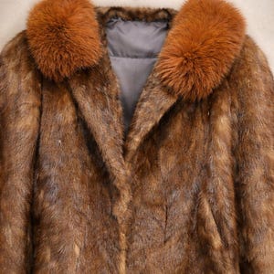 May include: A brown fur coat with a fox fur collar. The coat has a classic design with a notched collar and a long, flowing silhouette. The fur appears soft and luxurious, with varying shades of brown.
