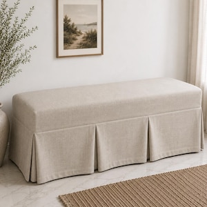 May include: A rectangular bench upholstered in a light beige fabric featuring a structured, box-pleated skirt that extends to the floor. The bench has a flat, cushioned top surface and a clean, uniform appearance with a consistent neutral color.