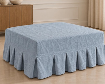 Peut inclure: Un pouf carré recouvert d'un tissu bleu clair à tissage texturé. La pièce présente une surface supérieure plate et une jupe plissée qui s'étend de la base jusqu'au sol, créant une apparence structurée et uniforme.