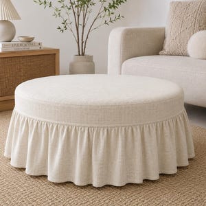 May include: A round, beige upholstered ottoman featuring a gathered, floor-length skirt. The ottoman is covered in a textured, woven fabric and has a flat, circular top surface. The base is fully concealed by the pleated fabric skirt.