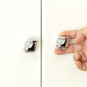 Pu&ograve; includere: Pomello per armadio cromato lucido con parte superiore arrotondata e base curva e decorativa. Il pomello &egrave; mostrato sia installato su un'anta bianca che tenuto in mano. L'hardware &egrave; progettato per l'uso su armadi, cassetti o altri mobili.