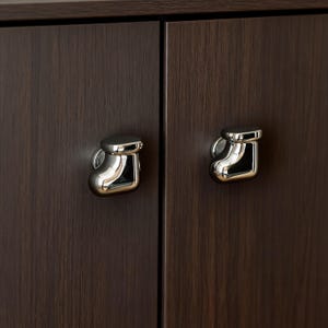 Pu&ograve; includere: Primo piano di due ante di armadio con pomelli per cassetti cromati abbinati. I pomelli hanno un design curvo unico e sono montati su ante con venature del legno marrone scuro. I pomelli sono lucidi e riflettono la luce.