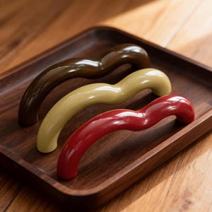 May include: Three curved handles in a wooden tray. The handles are in shades of brown, beige, and red. The handles have a glossy finish and a smooth, ergonomic design. The tray is made of dark wood.