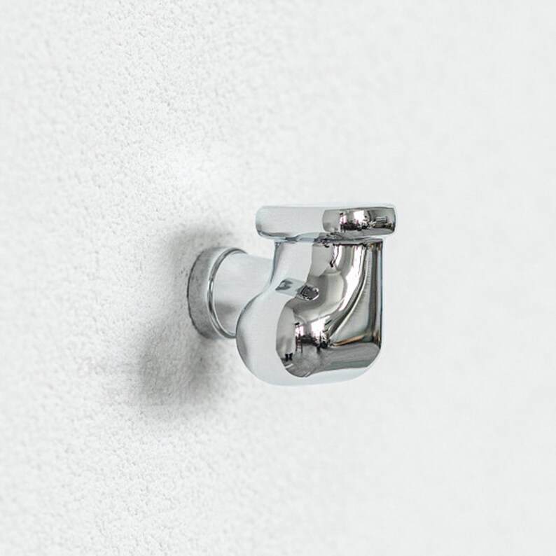 Pu&ograve; includere: Un raccordo idraulico cromato, progettato per il montaggio a parete. Il raccordo presenta un corpo curvo con una parte superiore rettangolare e una base circolare. Probabilmente fa parte di un sistema di approvvigionamento idrico.