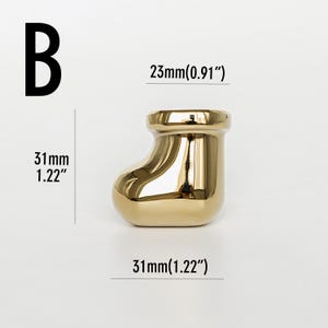 Pu&ograve; includere: Oggetto decorativo dorato a forma di stivale. Lo stivale &egrave; lungo e largo 31 mm e largo 23 mm. La lettera "B" &egrave; nell'angolo in alto a sinistra. Misure anche in pollici.