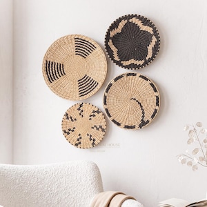 Peut inclure: Quatre paniers muraux ronds tressés présentant des motifs géométriques en beige naturel et noir. Les paniers varient en taille et sont disposés en groupe. Chaque pièce affiche une texture enroulée avec des formes sombres contrastées.