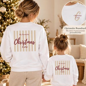 May include: Two white long-sleeve sweatshirts featuring a beige vertical striped square on the back with the text My favourite Christmas Crew in maroon. A circular inset shows a front chest print with a beige initial and text.