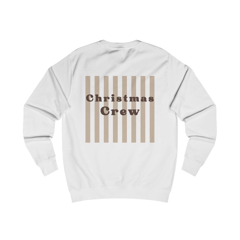 Puede incluir: Una sudadera blanca de manga larga con un gr&aacute;fico central de rayas verticales de color beige. Sobre las rayas aparece el texto "Christmas Crew" en una fuente serif redondeada, negrita y de color marr&oacute;n oscuro, en la espalda.