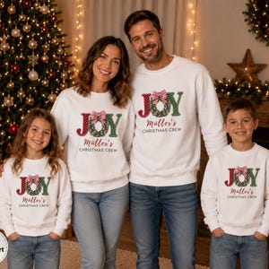 May include: Matching white crewneck sweatshirts featuring a graphic of a Christmas wreath forming the letter O in the word JOY, with a red and white gingham bow on top and the text M&auml;ller's CHRISTMAS CREW printed in red and black lettering.